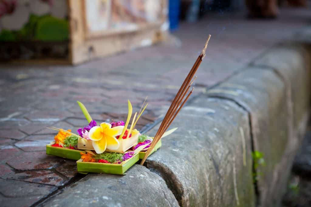 Traditional balinese offerings to gods in Bali with flowers and aromatic sticks